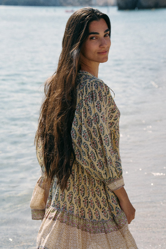 Side profile of woman at the water's edge wearing the Daughters of India Bhoomi Mini Dress in Meadow, showcasing the relaxed fit and sage green paisley print