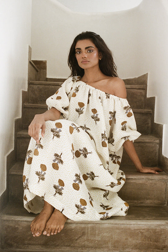 Dahlia Maxi Dress Marigold — seated on stone steps, off-shoulder, white hand block print linen maxi spread beautifully, romantic boho artisan dress from Jaipur | Daughters of India