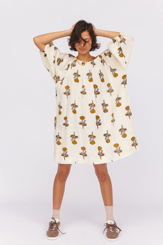 Dahlia Mini Dress Marigold — studio model full length, hands behind head pose, showing relaxed oversized silhouette, white linen with golden marigold hand block print, boho ethical linen dress | Daughters of India
