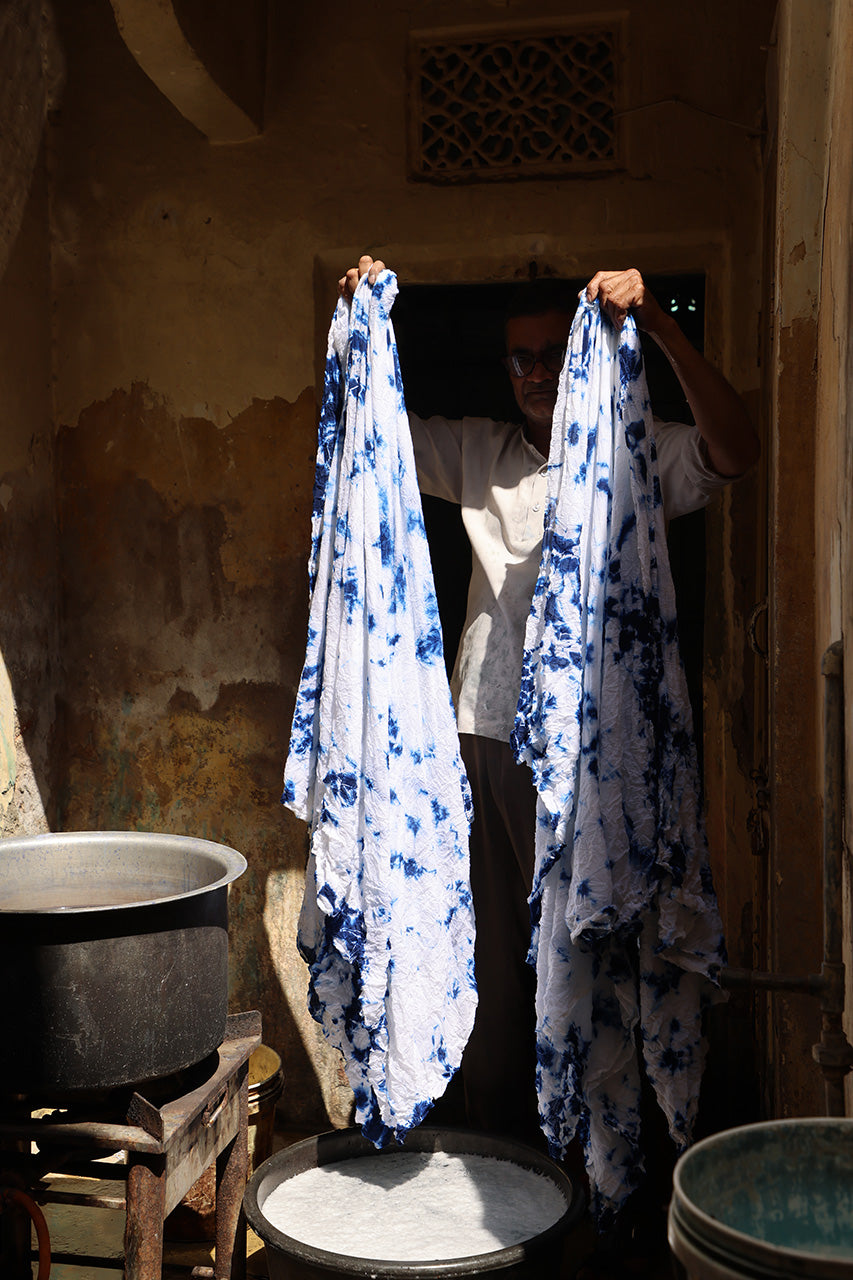 Kyra Maxi Dress Deep Sea — artisan holding up freshly dyed shibori tie-dye fabric in indigo dye workshop, traditional hand-dyeing process, Rajasthan India | Daughters of India