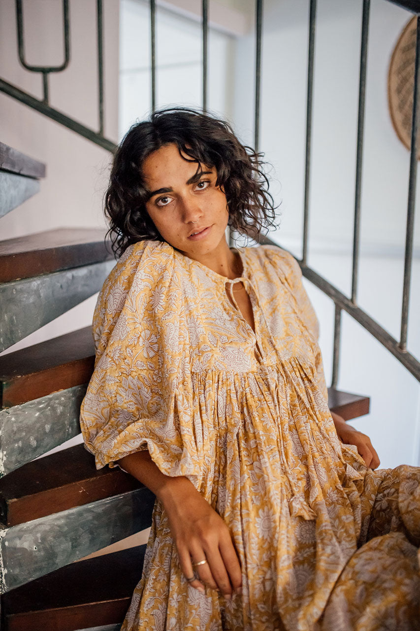 Daughters of India Kyra Midi Dress in Cumin — close-up neckline tie and billowed sleeves on staircase, hand screen print