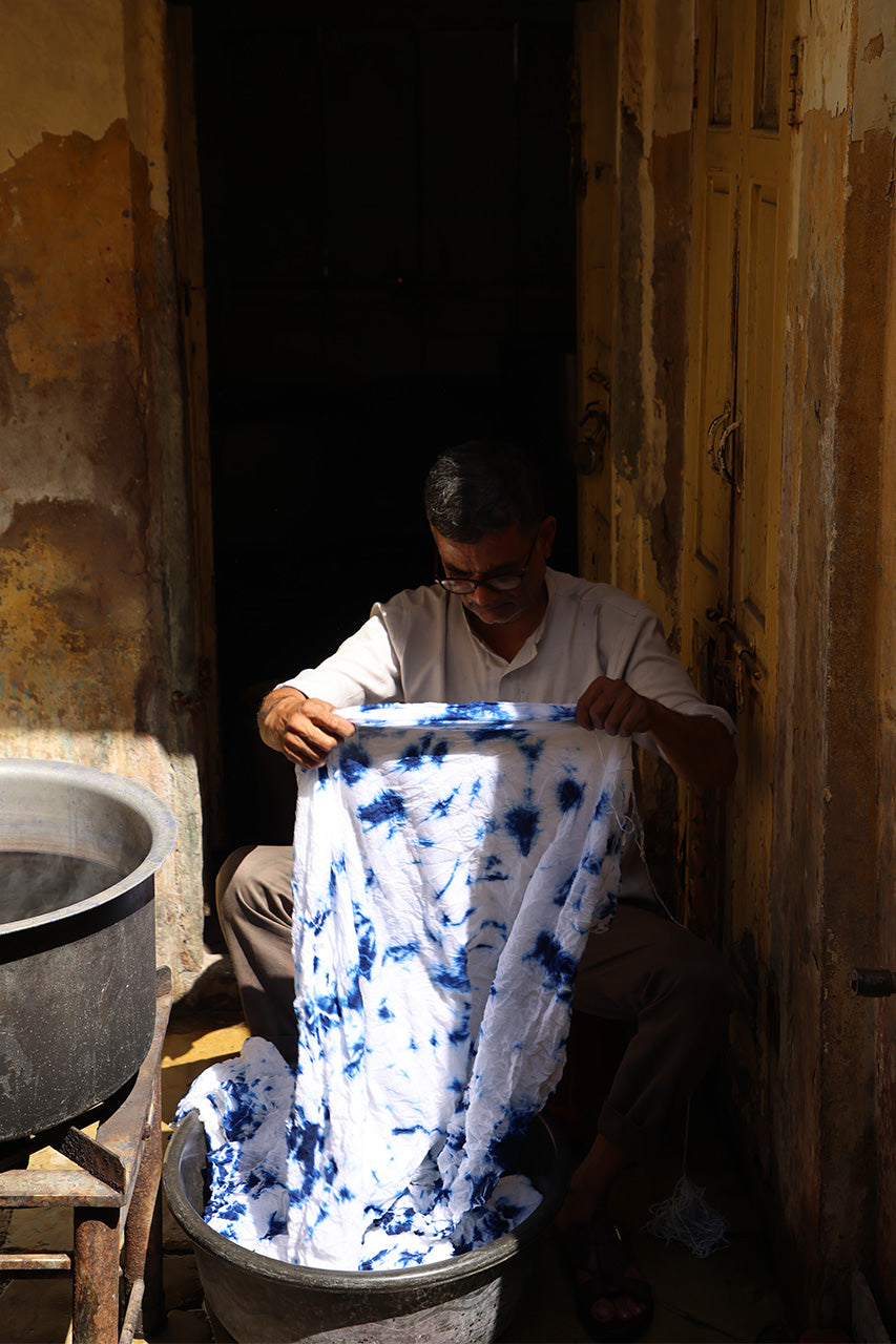 Kyra Midi Dress Deep Sea — artisan inspecting freshly dyed shibori tie-dye fabric in doorway of dye workshop, traditional hand-dyeing process, Rajasthan India | Daughters of India