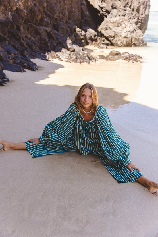 Ria Blouse Cyan Candy — overhead beach portrait, model reclining on sand wearing cyan and dark stripe hand block print cotton blouse, relaxed laid-back styling, artisan Jaipur India | Daughters of India