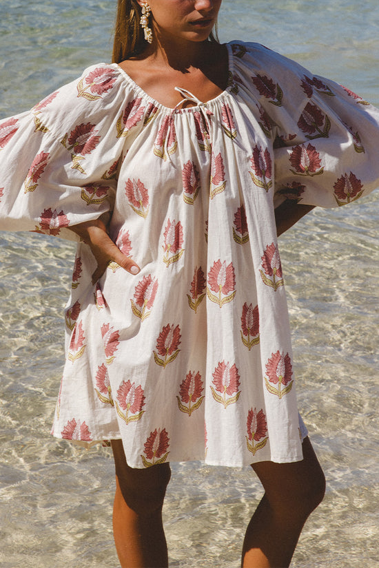 Ria Mini Dress Strawberry Cream — beach wading shot, model in shallow water wearing strawberry cream floral hand block print cotton mini dress, above-knee hemline, artisan Jaipur India | Daughters of India