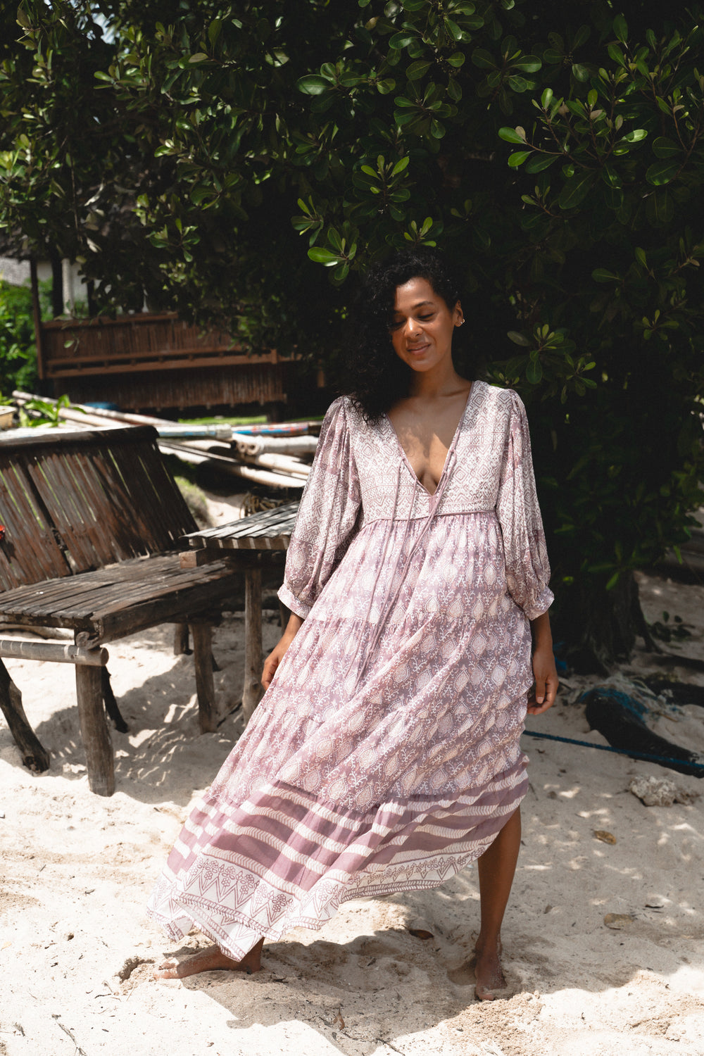 Jasmine Maxi Dress Lavender — outdoor lifestyle shot, model walking on sandy beach with tropical greenery, full skirt flowing in movement, hand block print lavender cotton maxi | Daughters of India