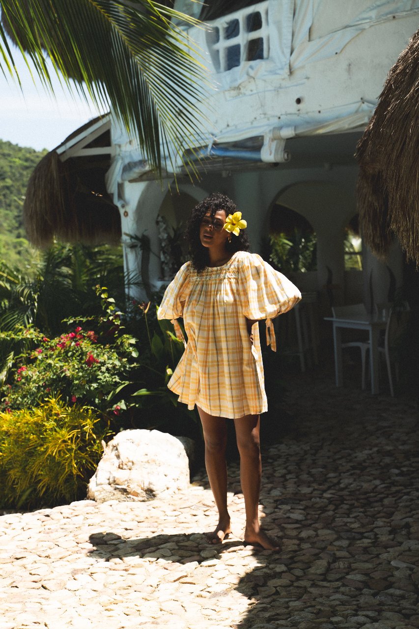 Freya Dress Honeycomb Plaid — full length outdoor shot by whitewashed villa, cobblestone path, flower in hair, handloom woven honeycomb yellow plaid mini dress, ethical artisan fashion | Daughters of India